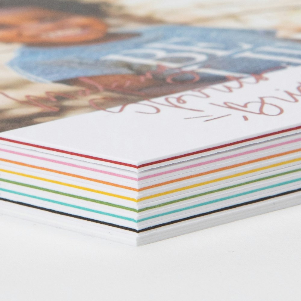 Close-up corner detail of a stack of Triple Thick Flat Cards showing all of the color insert options: white, black, teal, green, yellow, orange, pink, and red.