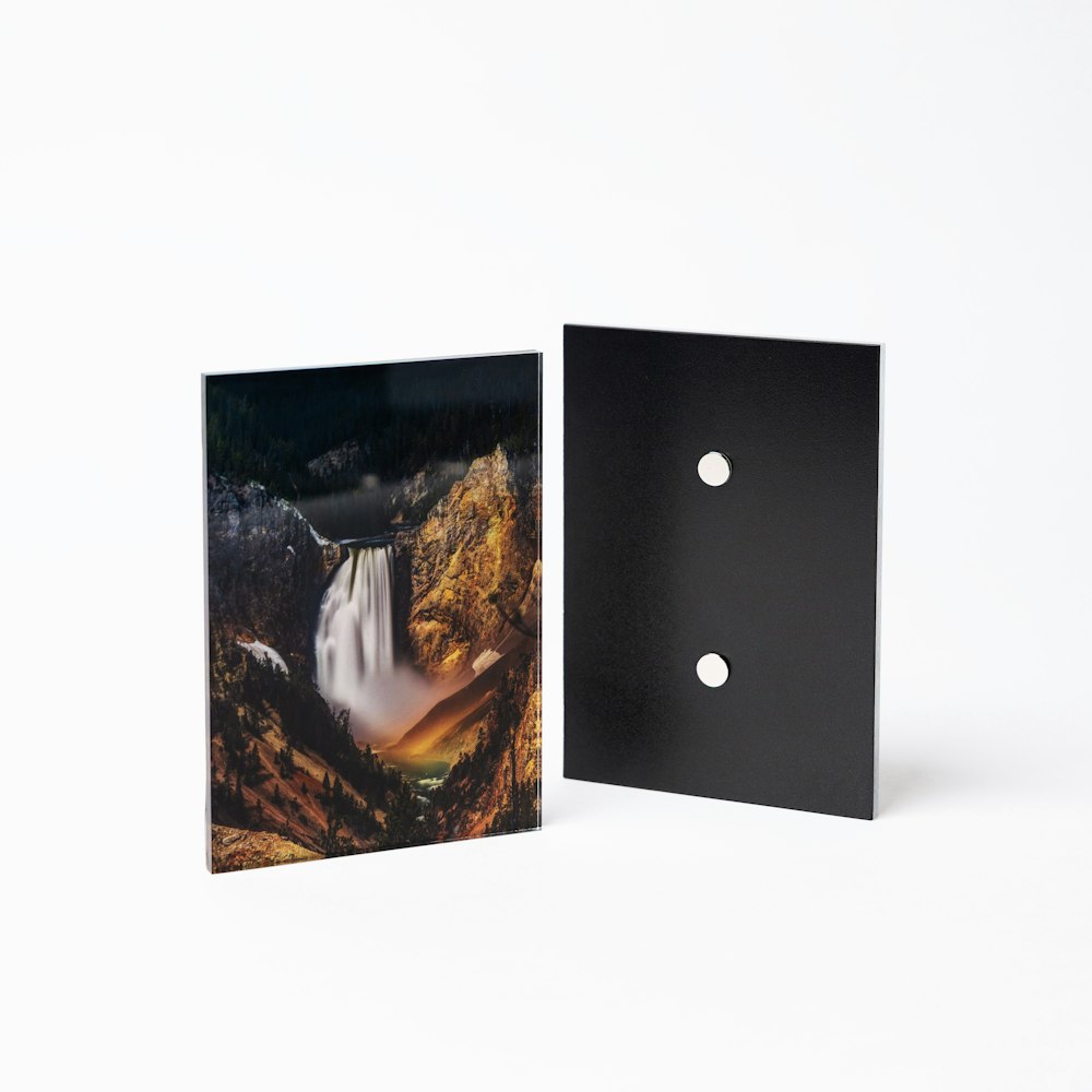 Two 5×7 Acrylic Prints with Magnet Back display hardware standing up on white background, front view shows a waterfall landscape image and back view shows two round magnets
