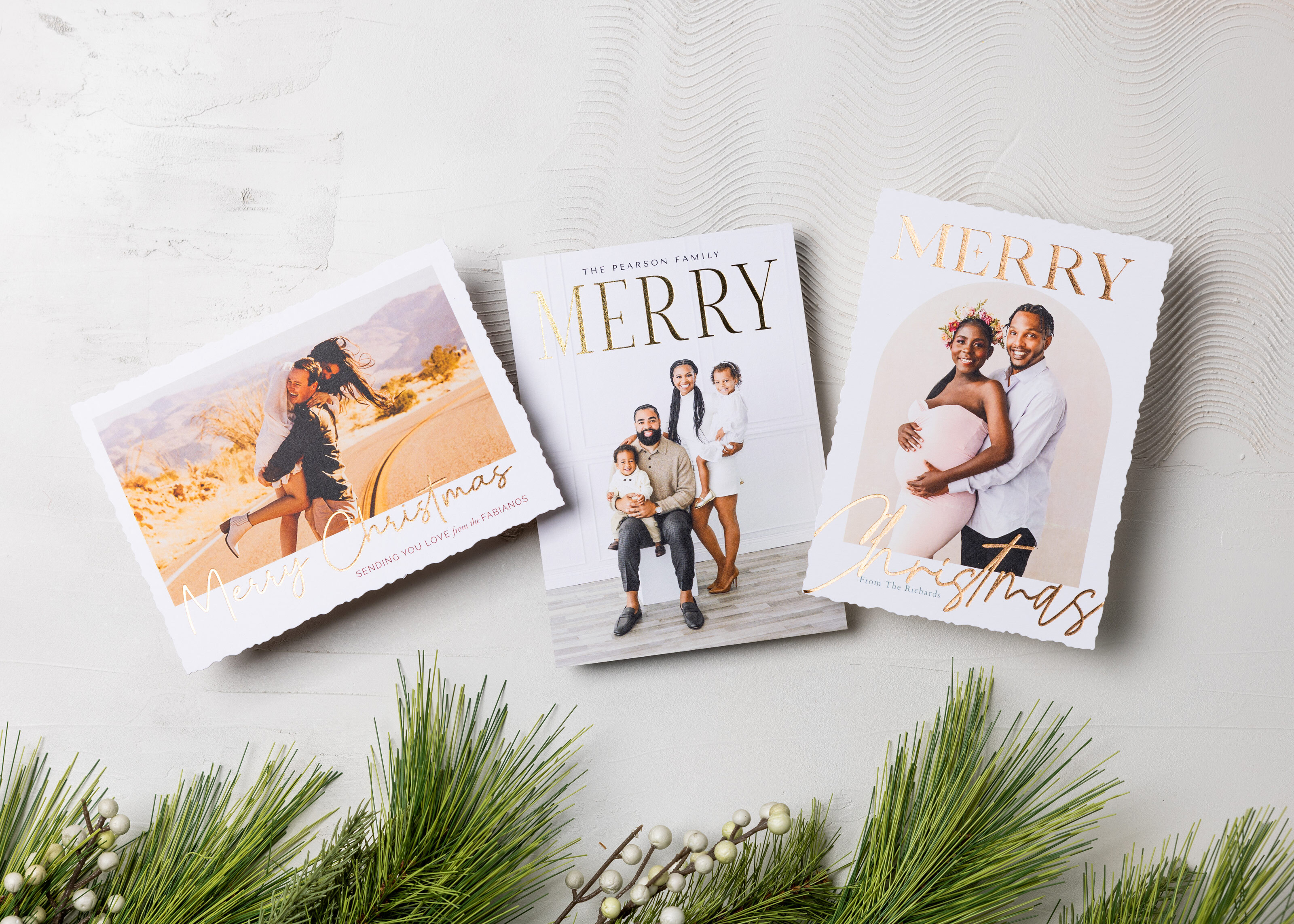 Three foil-pressed 5×7 Flat Cards featuring wedding, family, and maternity portraits on an off-white textured background with pine branches along the bottom