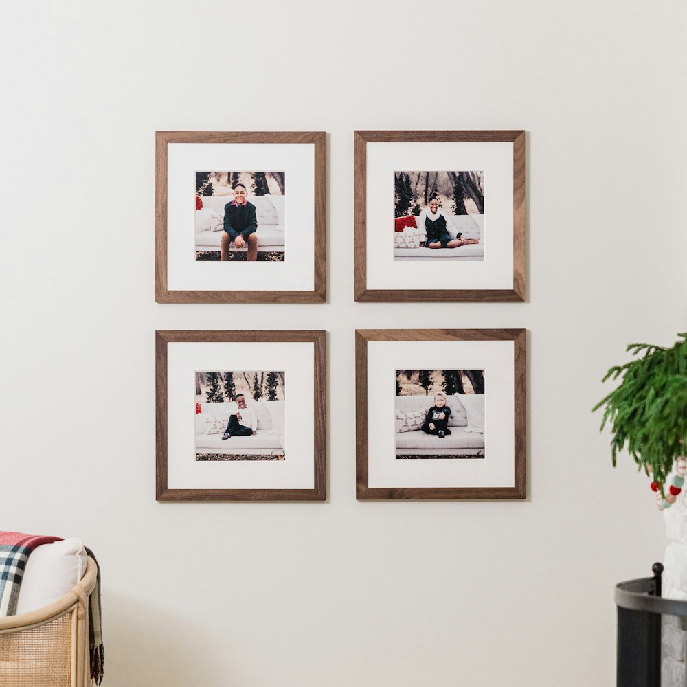 Grid wall collage of four square Walnut Woodland Framed Prints with mats hung on living room wall with fireplace and holiday garlands, featuring holiday-themed portraits of the family's children