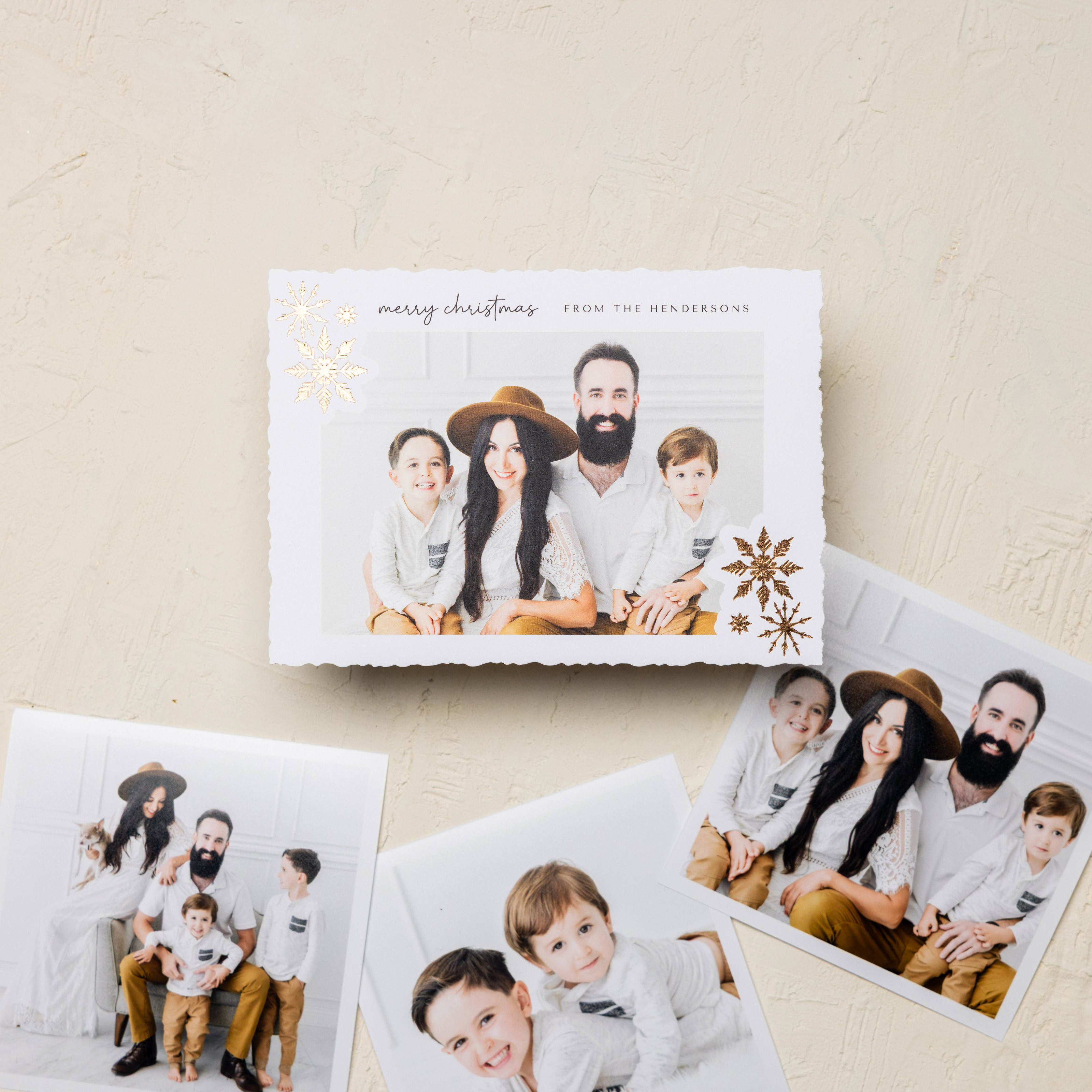 Gold foil snowflake design on the corners of a 5x7 holiday Flat Card that reads "Merry Christmas from the Hendersons" and features professional family portraits in a modern studio