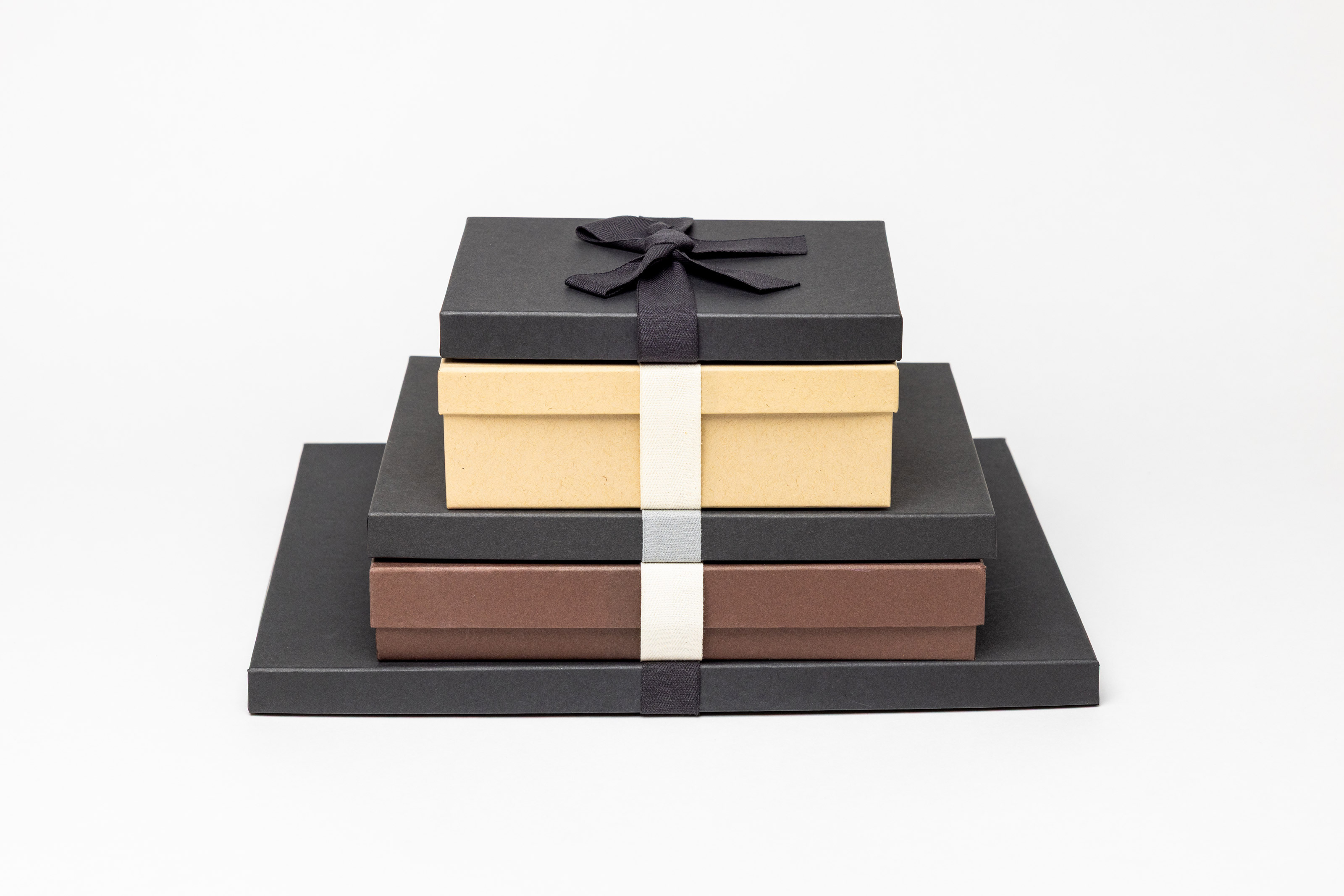 Multiple Premium Packaging boxes in several sizes, stacked from largest to smallest, with a few color options, such as Charcoal with Black Ribbon, Kraft with Cream Ribbon, and Brown with Cream Ribbon.
