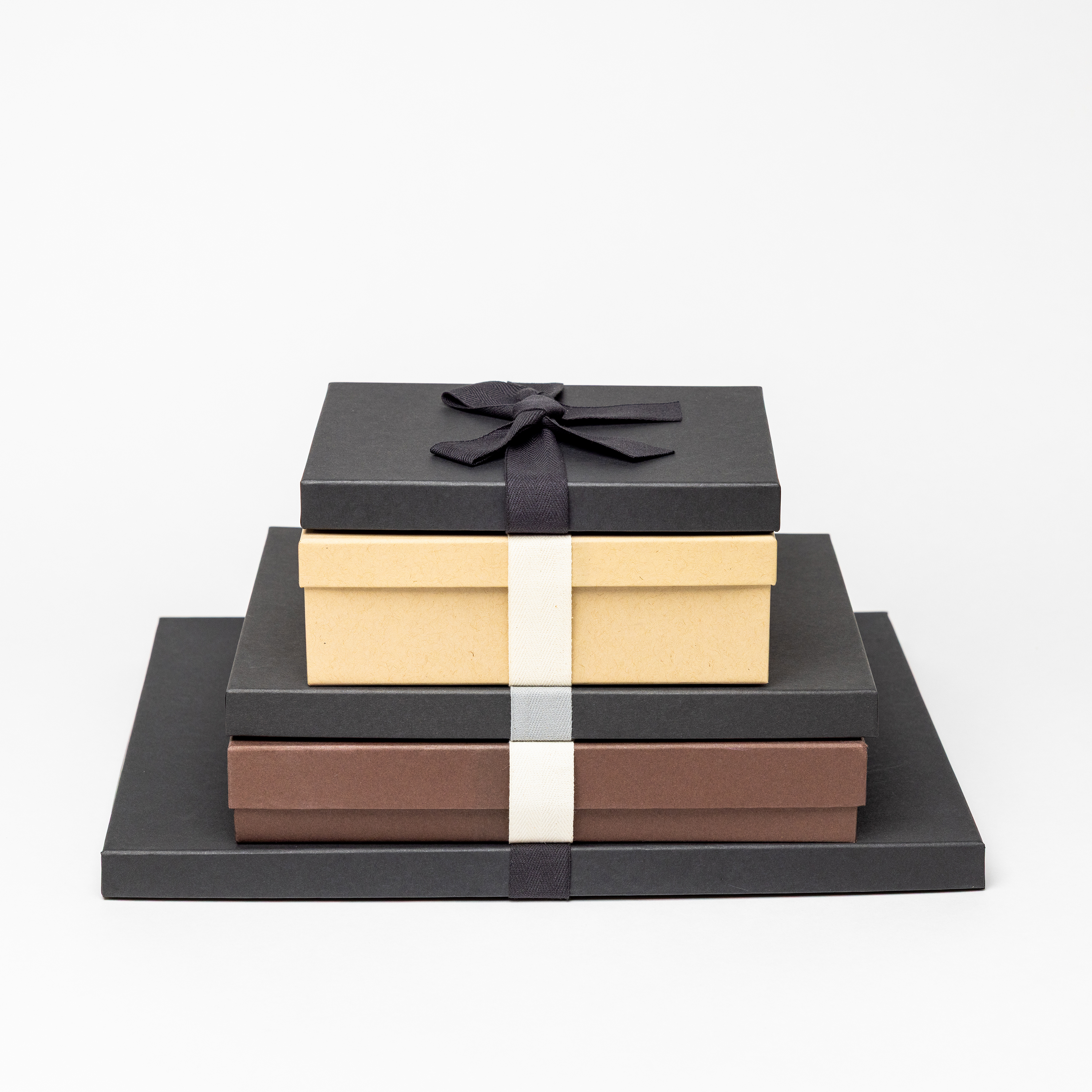 Multiple Premium Packaging boxes in several sizes, stacked from largest to smallest, with a few color options, such as Charcoal with Black Ribbon, Kraft with Cream Ribbon, and Brown with Cream Ribbon.