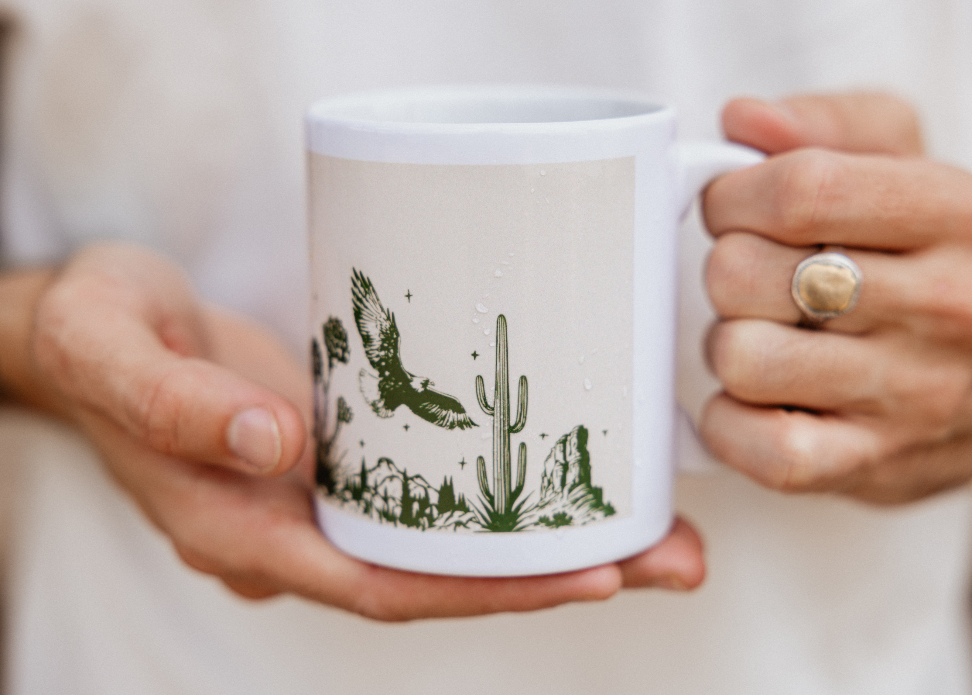 Close-up of hands with ring holding a custom printed mug with an illustration design