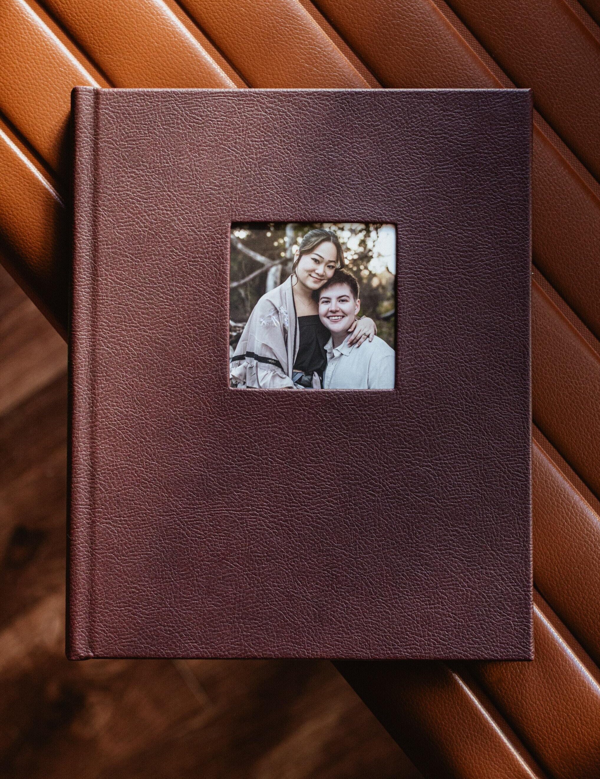 Closed merlot leatherette layflat guest book with a cameo cutout cover framing an engagement portrait of a couple.