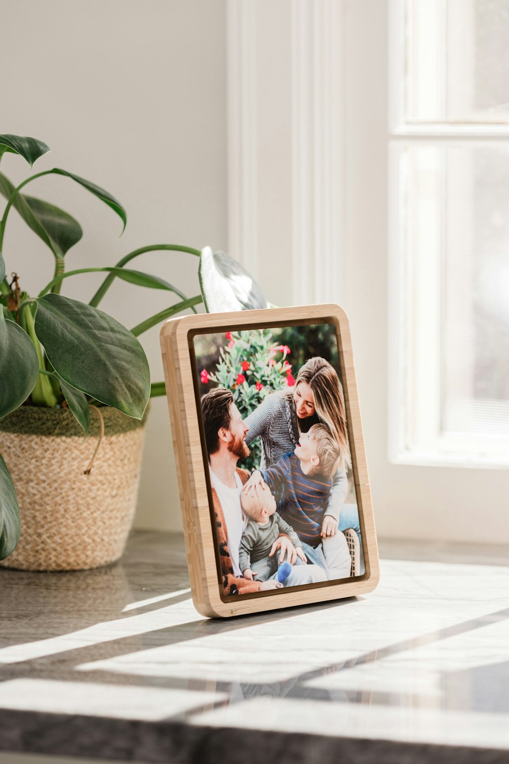 Candid family photo printed on a 5x7 Metal Print in a Bamboo Tabletop Frame, placed on a stone counter next to a window with sunlight streaming in