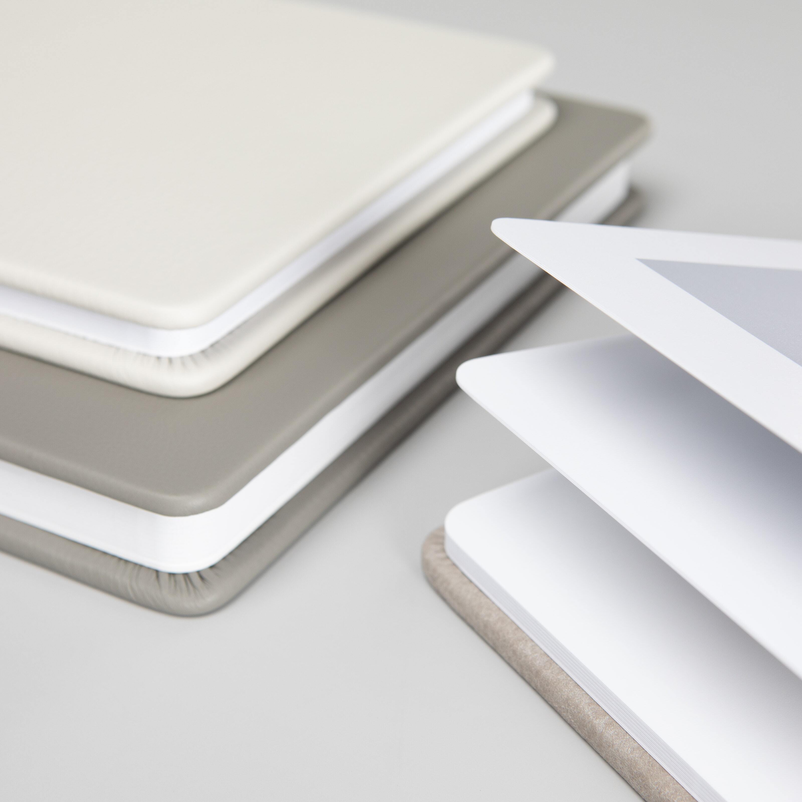 Stacked professional photo albums with rounded corners in premium leather covers showing thick lay-flat spreads.