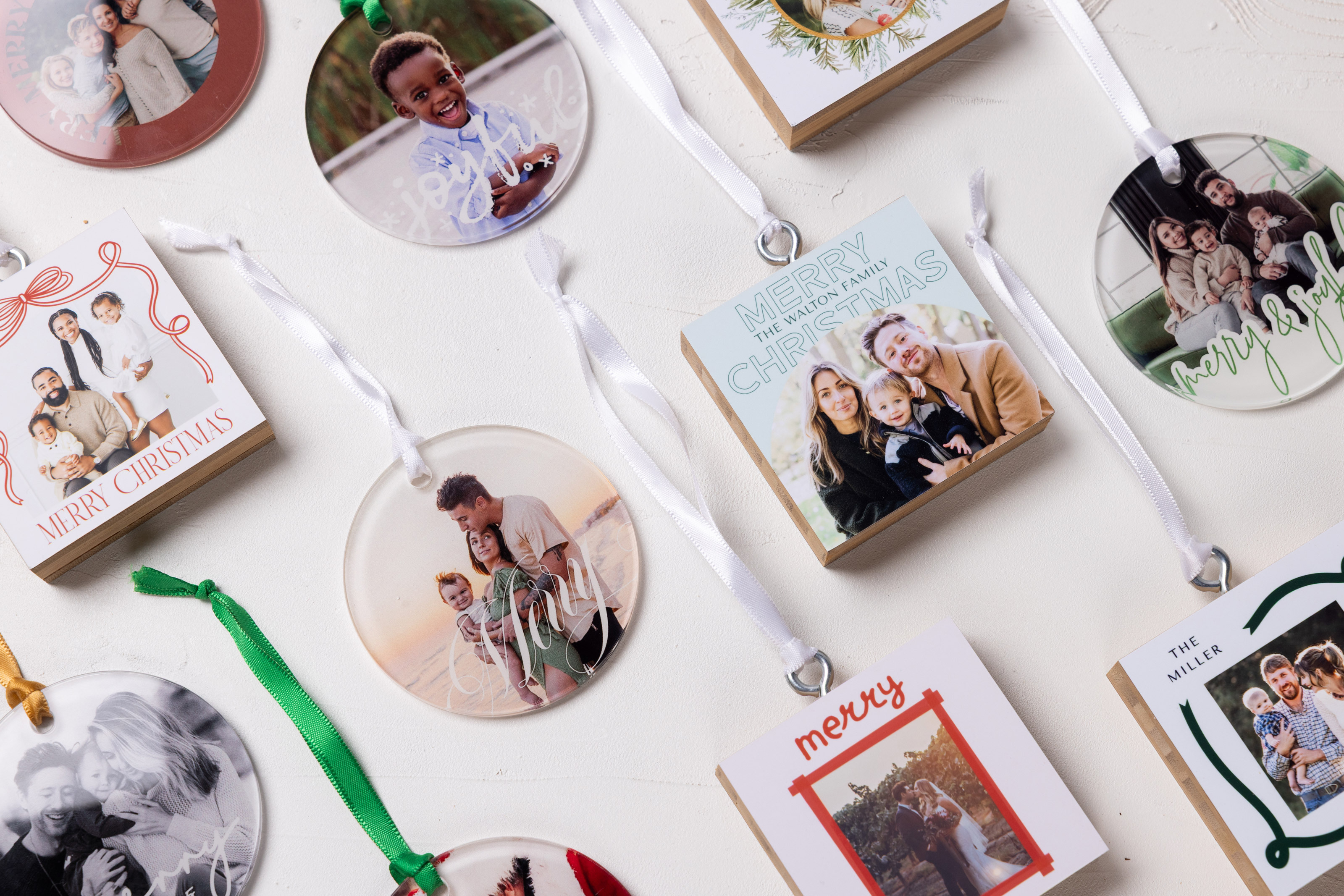 Flatlay of multiple Bamboo and Acrylic Ornaments arranged in an angled grid on a white, textured background. Each custom-printed ornament features professional portrait photography from family sessions and weddings.