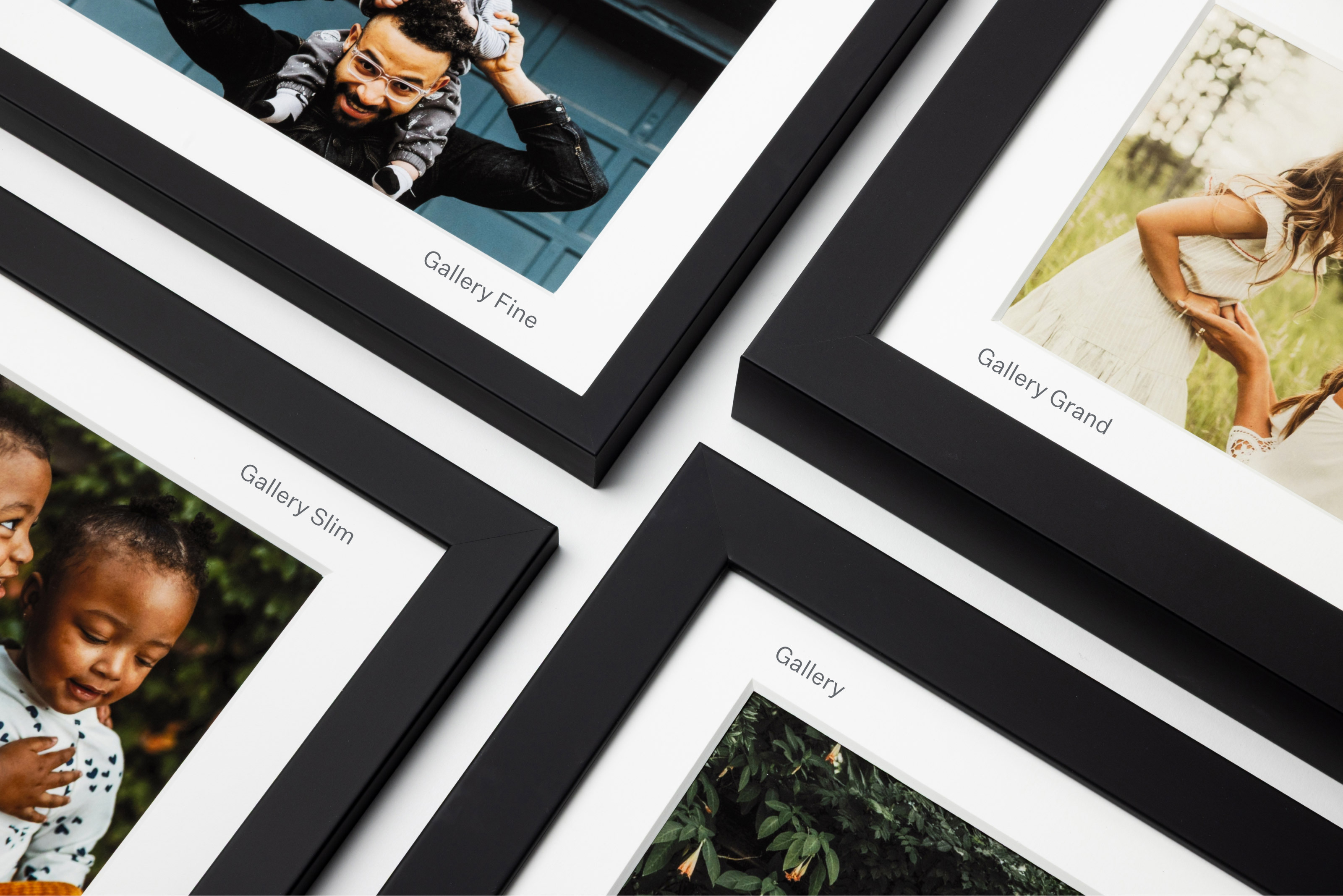 Four professional framed and matted family portrait photographs arranged in a square formation, each demonstrating the four Gallery frame moulding profile sizes for comparison. The top left frame is labeled Gallery Fine, top right is Gallery Grand, bottom left is Gallery Fine, and bottom right is Gallery.