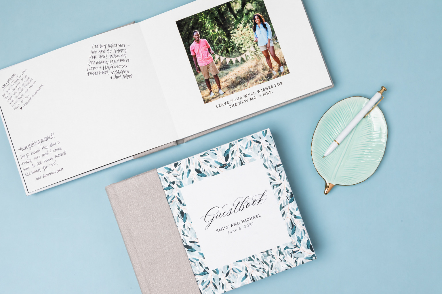 Open layflat wedding guest book showing handwritten well-wishes beside an engagement photo, with a linen combo covered “Guestbook” closed below.