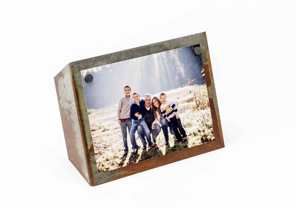 A family photo featuring two adults and three children outdoors is displayed in a rustic metal frame with a slanted design.