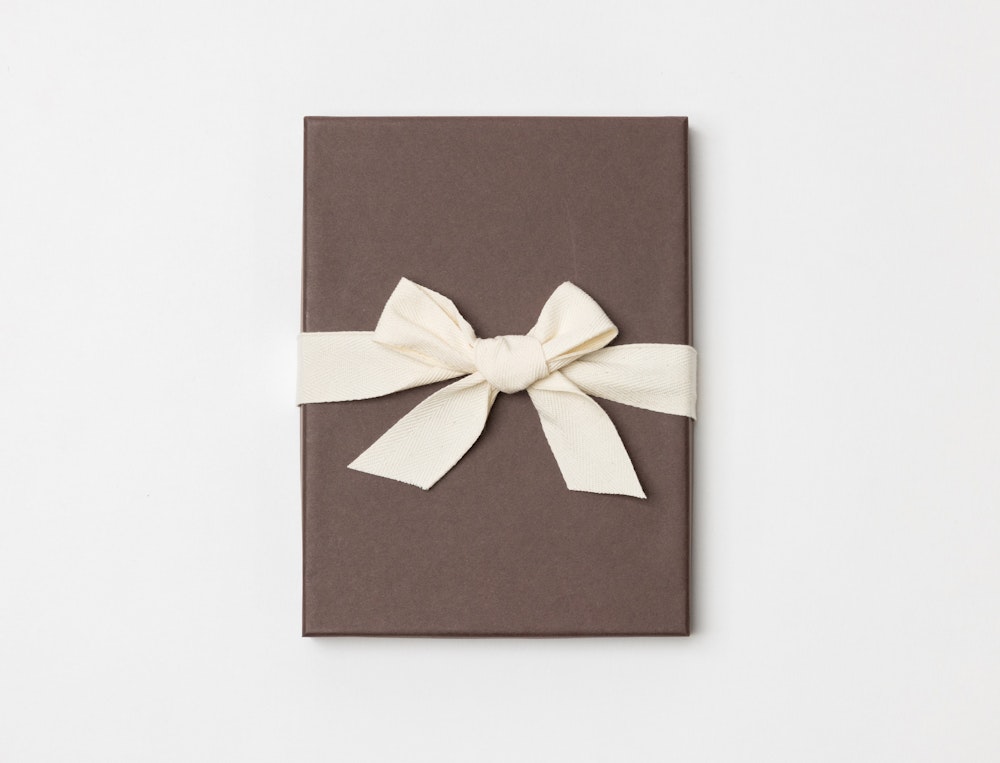 Brown Premium Packaging box with a cream ribbon tied in a bow on a light gray background
